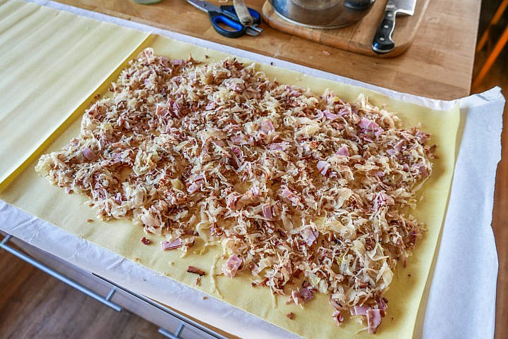 Fertiger Nudelteig mit einer Sauerkraut-Speck-Mischung wird aufgerollt. 